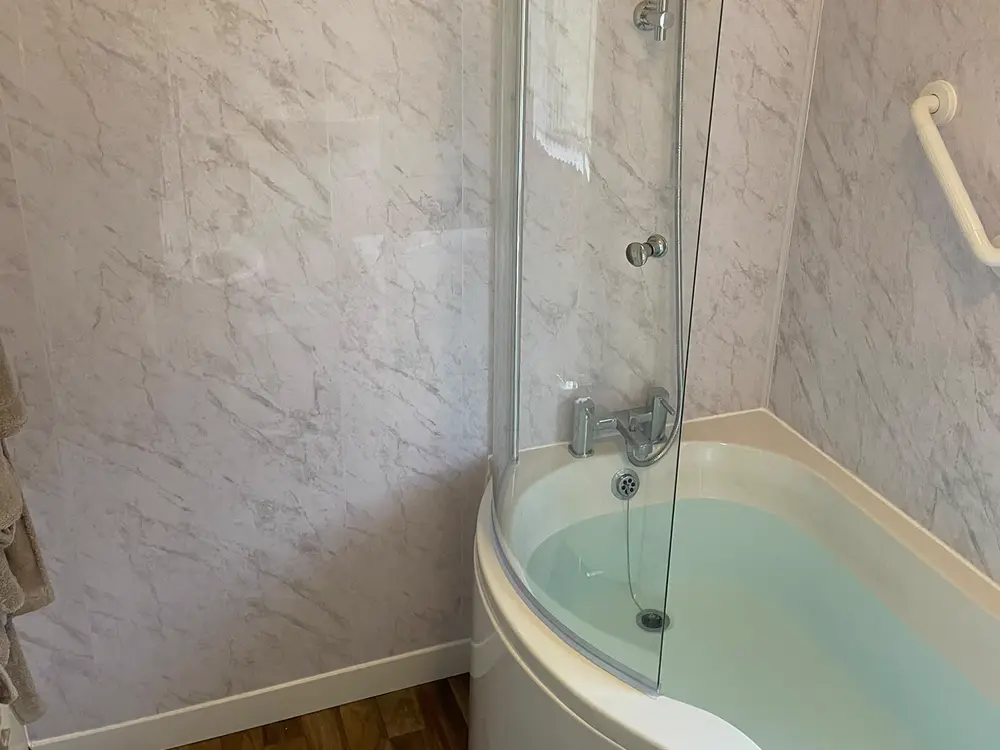 P-shaped shower bath with a glass screen and white marble-effect wall panels