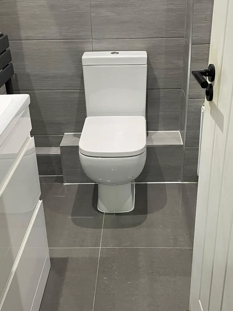 Close-coupled toilet and white vanity unit with large grey floor and wall tiles
