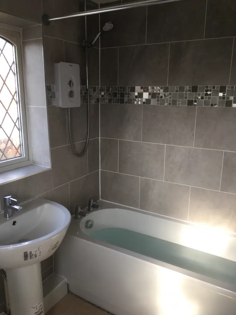 Bath, pedestal basin and grey tiling with a mosaic border under a leaded window