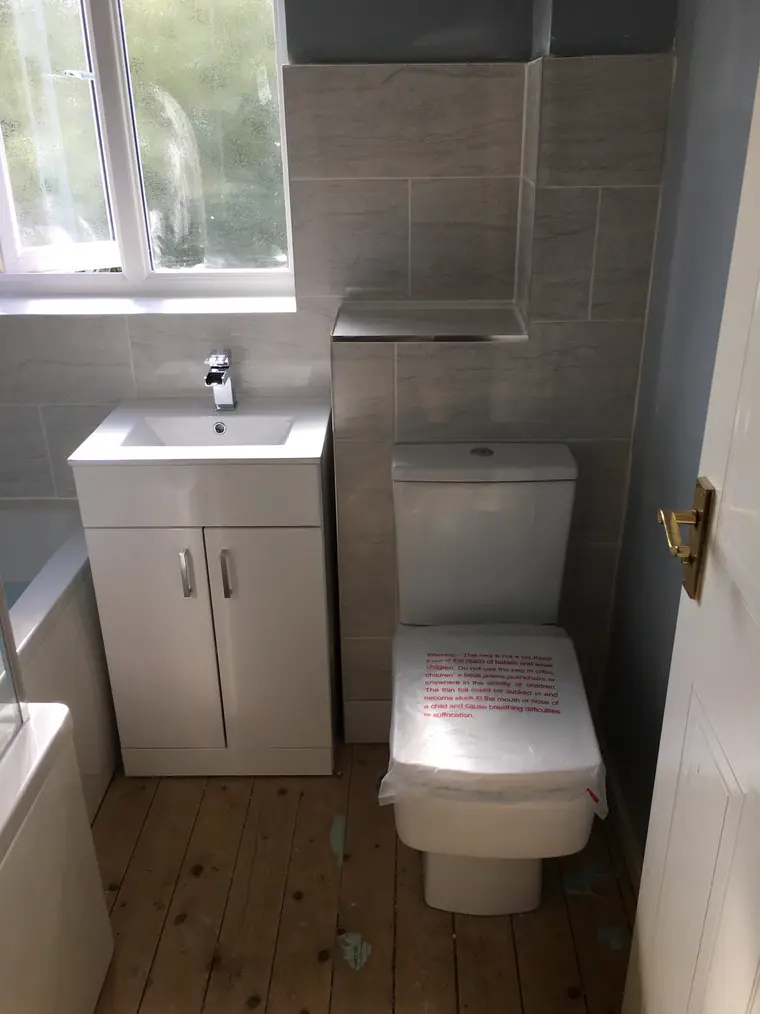 Vanity basin unit and toilet under a window with grey wall tiles