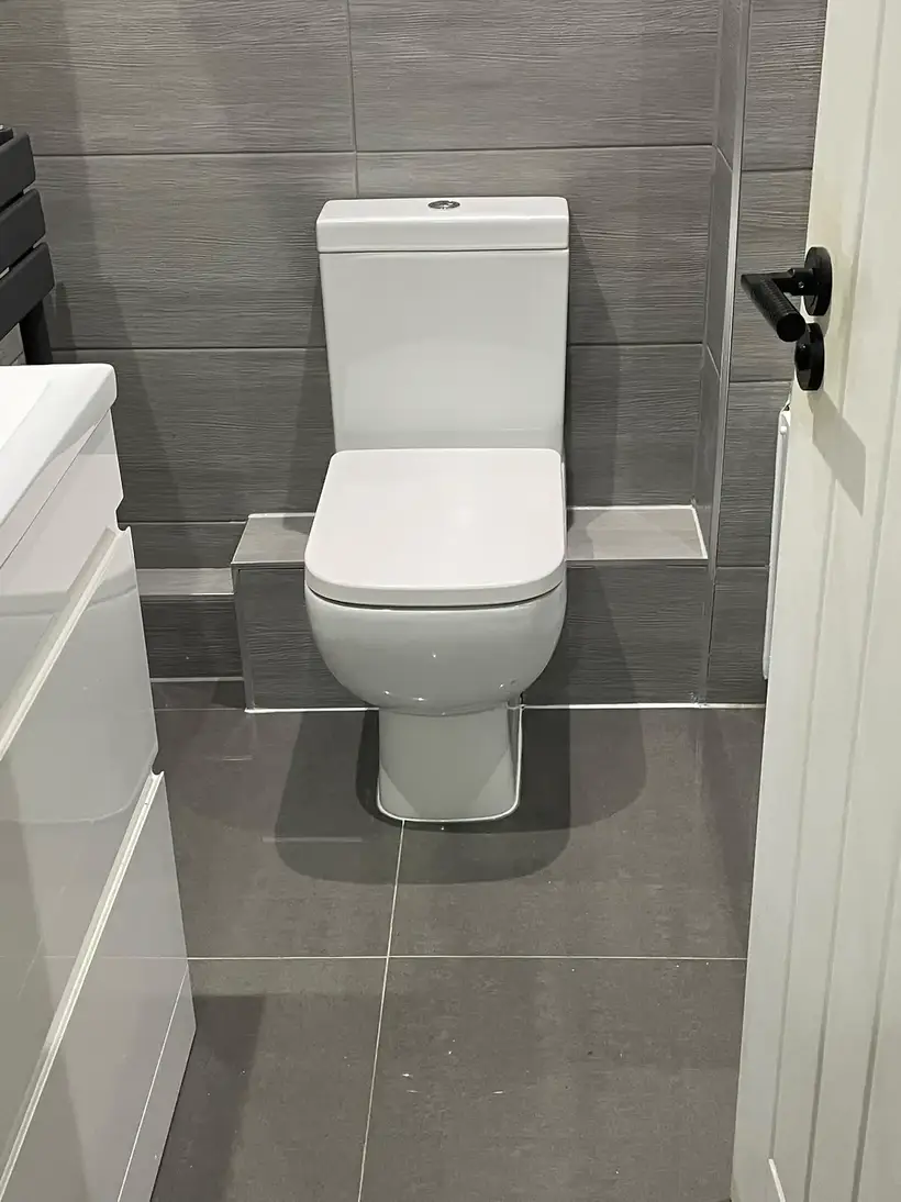 Close-coupled toilet and white vanity unit with large grey tiles on the floor and walls