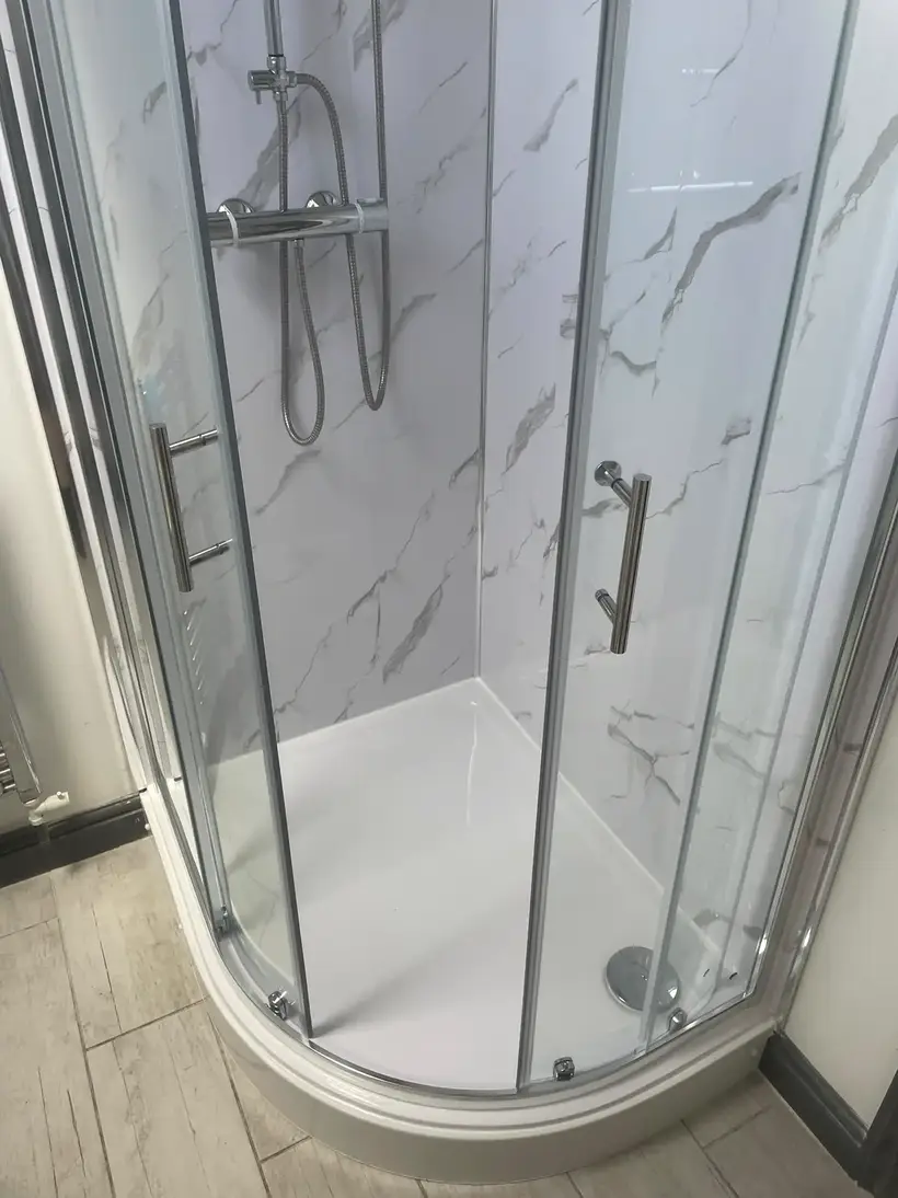 Quadrant shower enclosure with sliding glass doors against white marble-effect wall panels