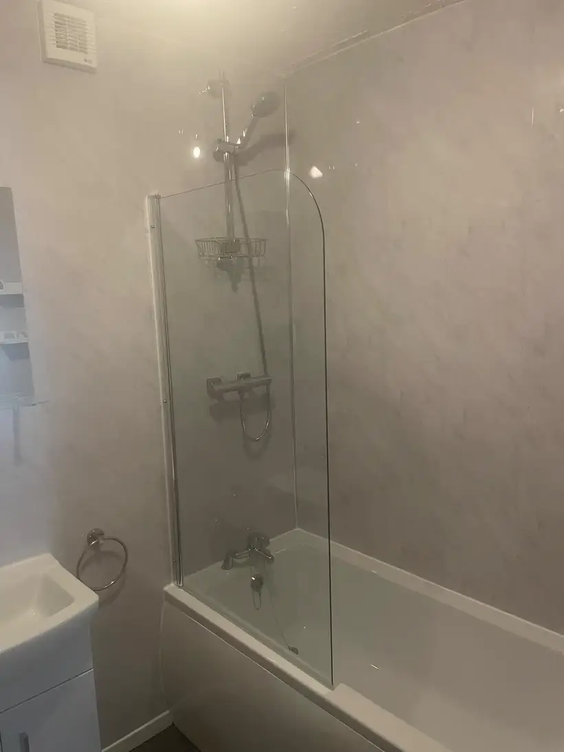 Bath with a glass shower screen and a pedestal basin, light marble-effect wall panels
