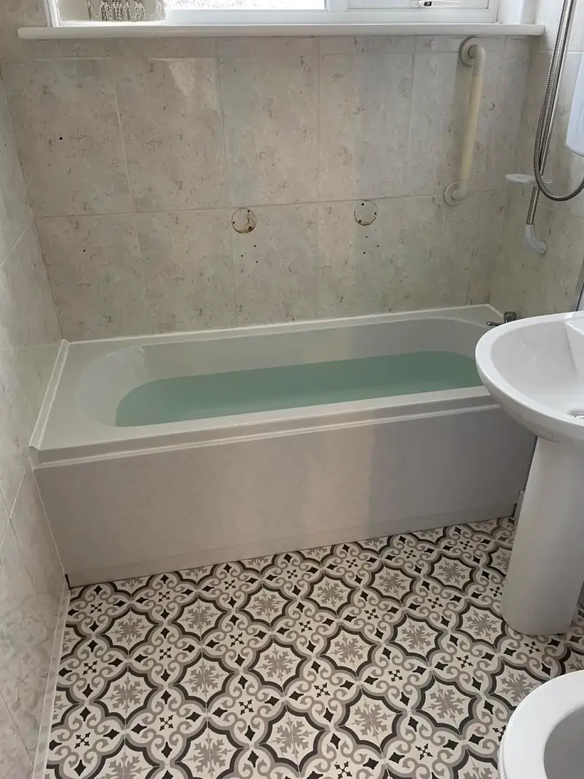 White bath and pedestal basin with marble-effect walls and a patterned grey and white floor tile