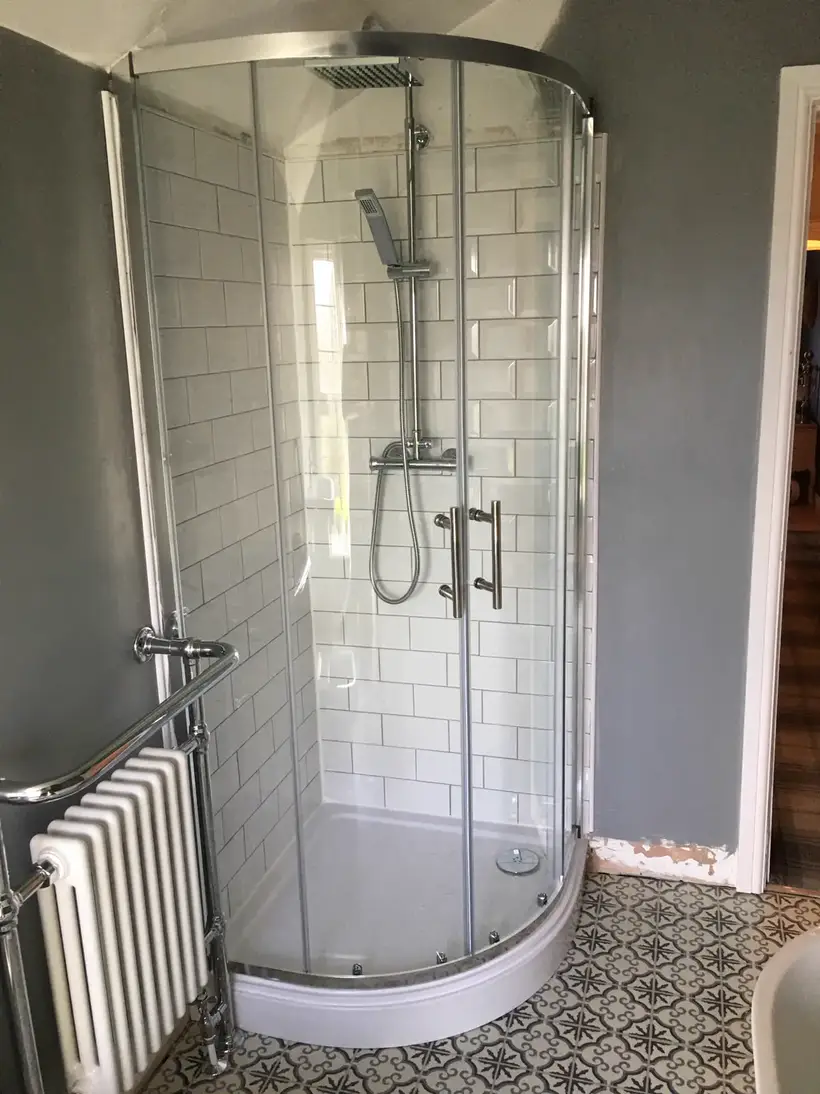 Quadrant shower enclosure with white metro wall tiles beside a chrome column radiator