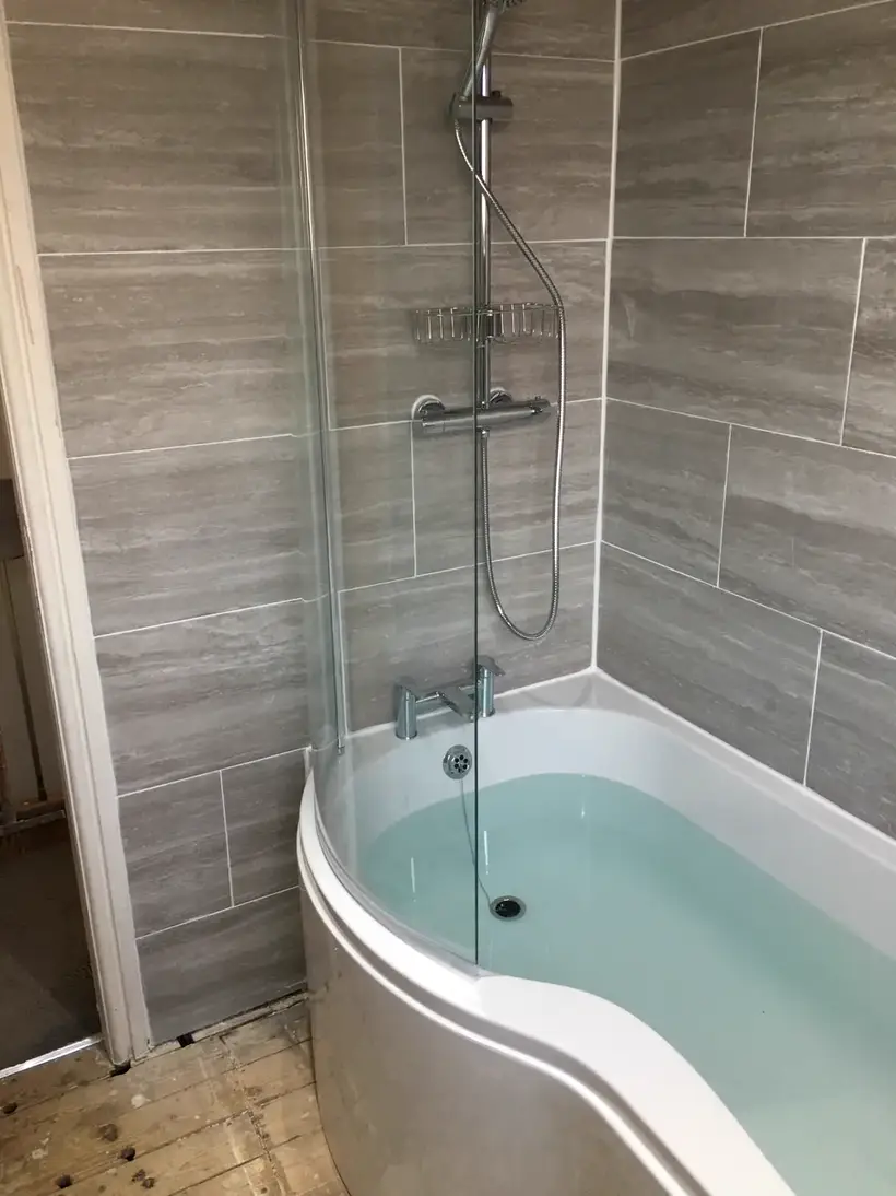 P-shaped shower bath with a glass screen and grey wood-effect wall tiles