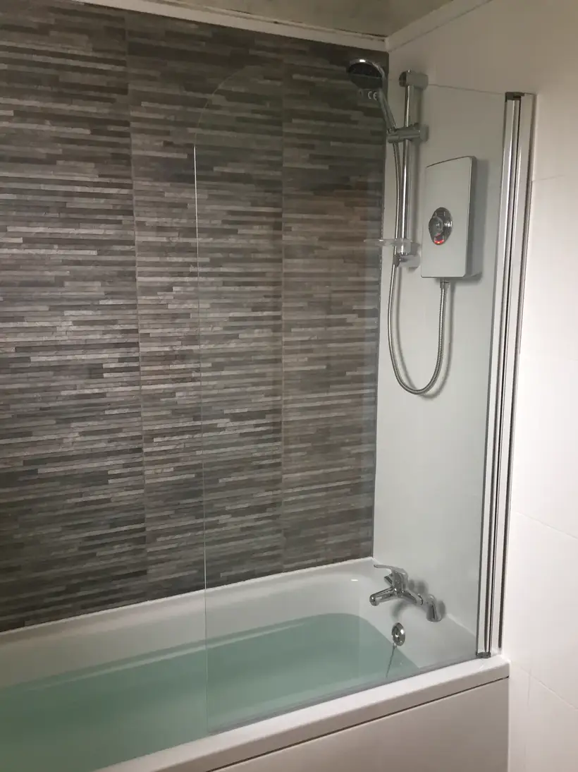Bath with an electric shower and glass screen, grey linear mosaic wall tiles