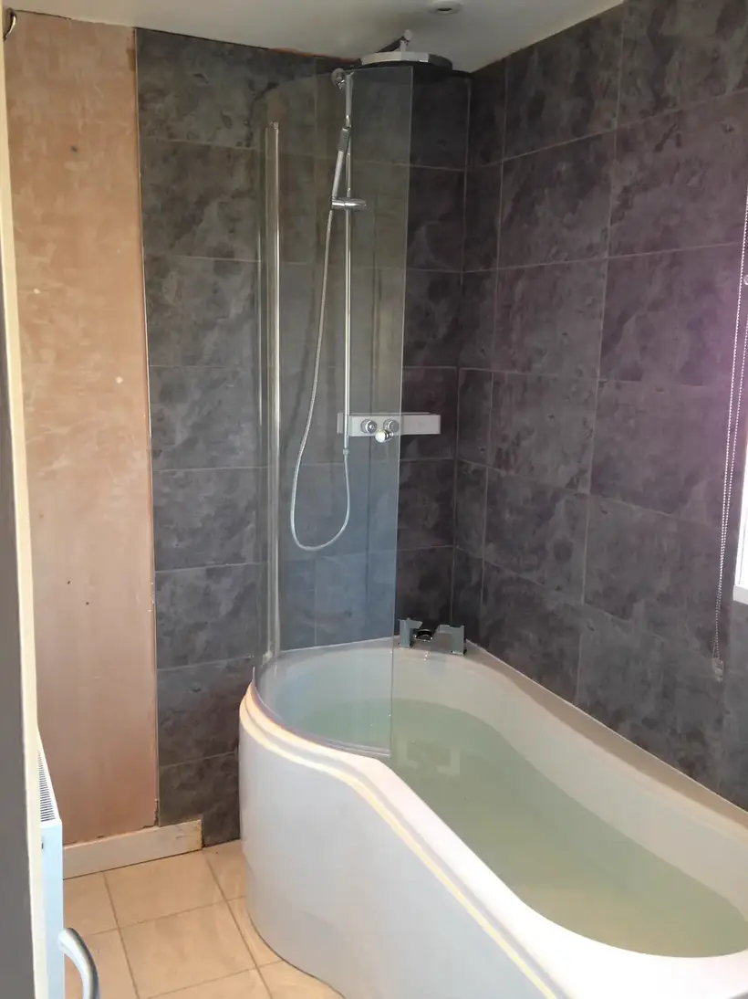 P-shaped shower bath against dark marble-effect wall panels