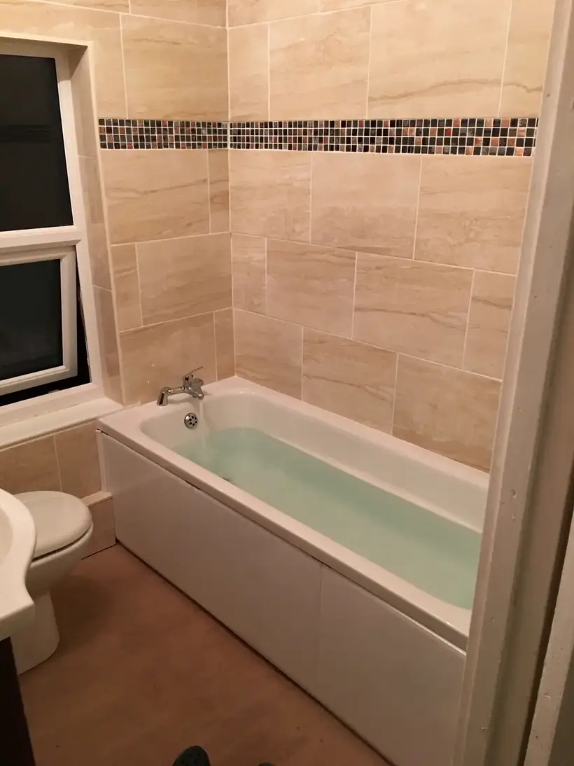 Bath and toilet in a room tiled in cream with a mosaic border