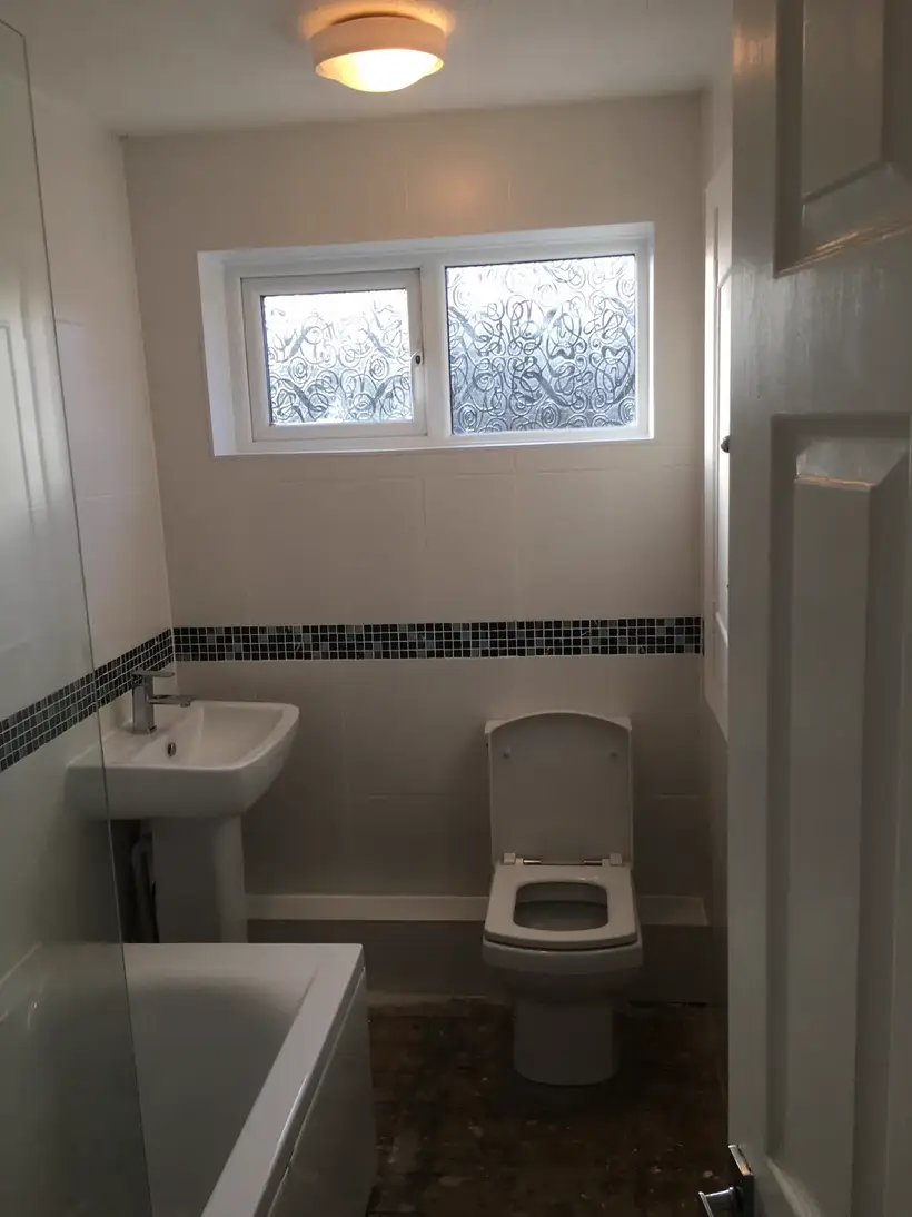 Pedestal basin and toilet with cream tiles and a mosaic border under the window