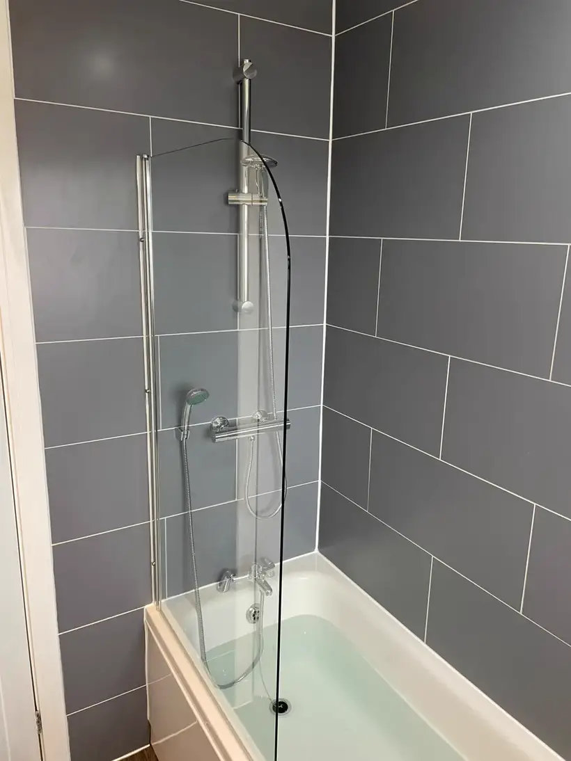 Straight bath with a curved glass shower screen against large grey wall tiles