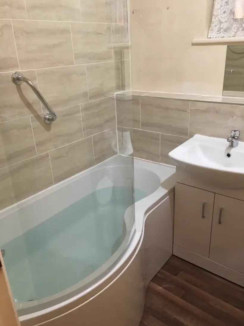 P-shaped shower bath with a glass screen beside a white vanity unit, stone-effect wall tiles