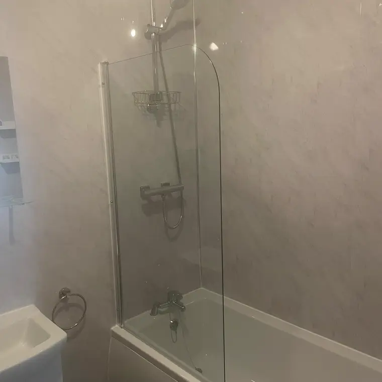 Finished bathroom with a bath, glass shower screen and marble-effect wall panels