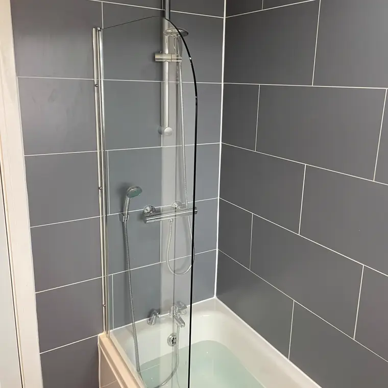 Straight bath with a curved glass shower screen against large grey wall tiles