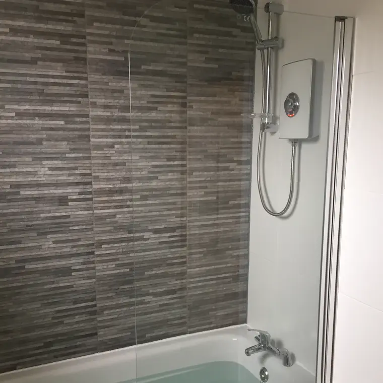 Grey linear mosaic tiling around a bath with a shower over it