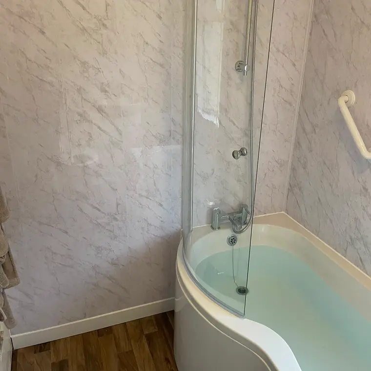 P-shaped shower bath with a glass screen and white marble-effect wall panels