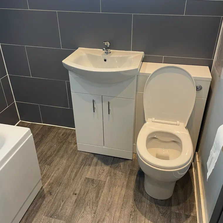 White vanity basin unit and toilet against dark grey wall tiles