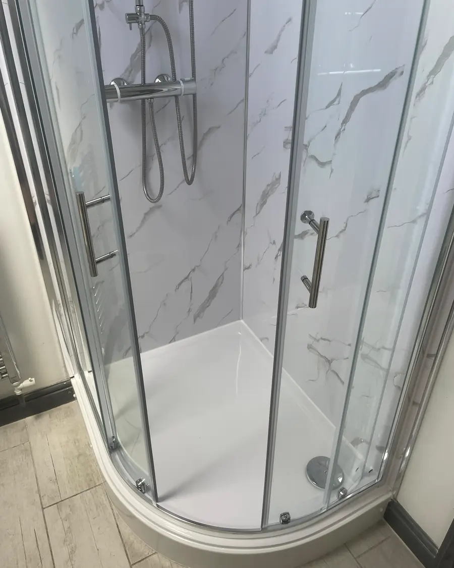 Quadrant shower enclosure with white marble-effect wall panels and a wood-effect floor