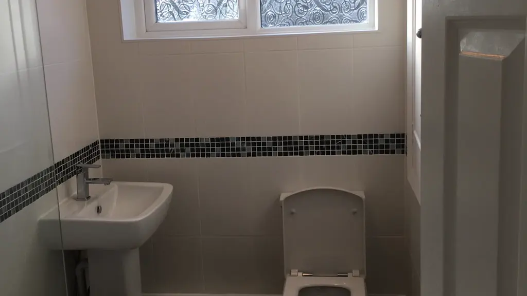 Finished bathroom with a pedestal basin, toilet and cream tiles with a mosaic border under the window
